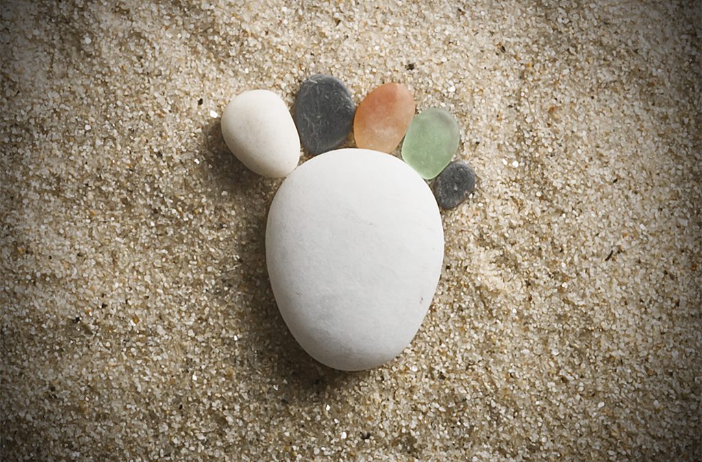 Una piedra grande blanca con cinco piedras ordenas por tamaños sobre la arena. Crean la forma de un pie.
