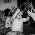 Tres niños con las manos en alto, riendo en la sala de una casa.