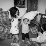 Tres niños peleando con cojines en la sala de una casa.