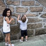 Una foto con un niño tocando una pared y la niña girada mirando a la cámara.