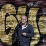 Un señor encendiendo un cigarro junto puerta de metal cerrada con pintadas.